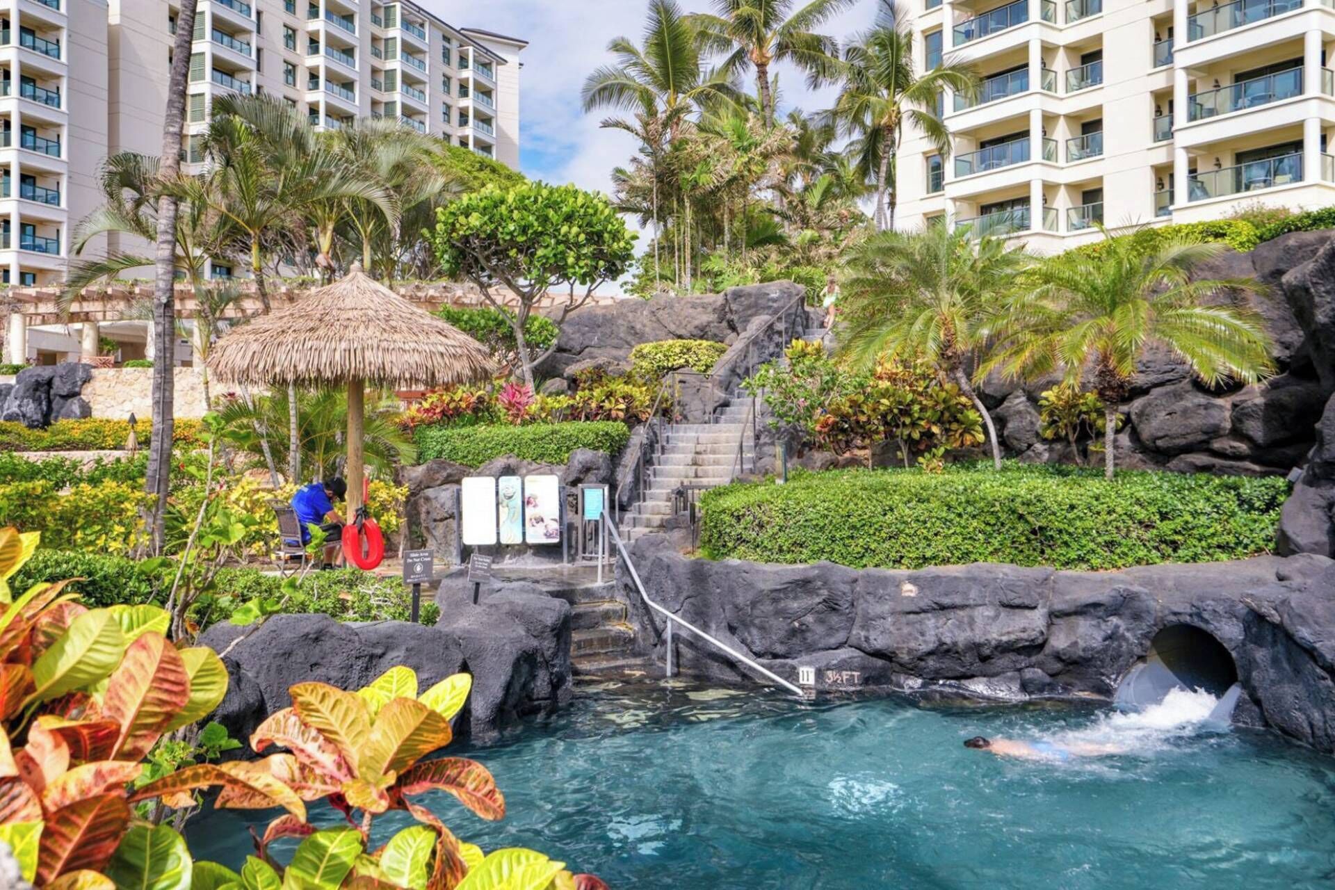 Un resort con piscina, una estructura de techo de paja y una escalera que lleva a un nivel superior.
