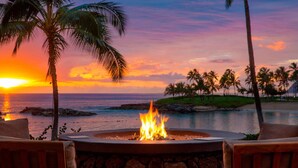 A fire pit with a view of the ocean and palm trees at sunset.