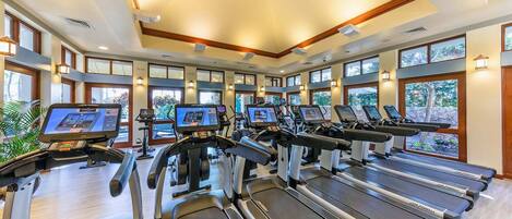 Un gimnasio con cintas de correr, bicicletas estáticas y elípticas, amplias ventanas y un diseño de techo moderno.