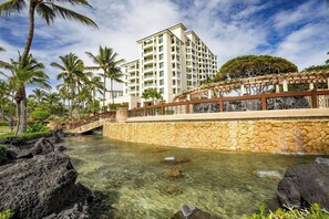Um resort com piscina cristalina, uma ponte de pedra e um edifício com várias andares e sacadas.
