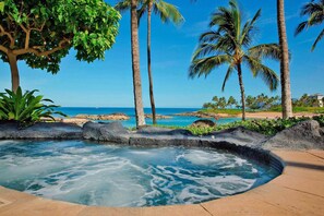 Uma banheira de hidromassagem rodeada por plantas tropicais e palmeiras, com vista para uma praia e águas azul-claras.