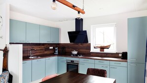 Een moderne keuken met lichtblauwe kastjes, een donker houten aanrecht, een hanglamp en een raam met uitzicht op een zeilboot.