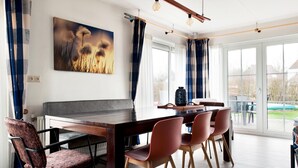 Een eethoek met een houten tafel en stoelen, een schilderij aan de muur en een uitzicht door grote ramen.