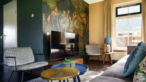 Un salon moderne doté d’un grand téléviseur à écran plat, de deux fauteuils à motifs, d’un canapé, d’une petite table ronde et d’une fenêtre avec des rideaux.