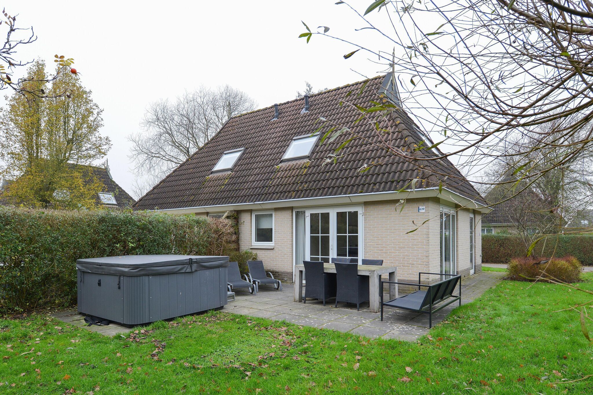 A house with a tiled roof, a patio with a table and chairs, and a hot tub.