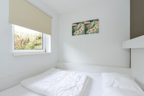 A room with a bed, a window with a view of greenery, and two floral paintings on the wall.