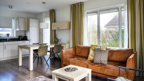 A modern living room with a brown leather sofa, a dining table with chairs, and a kitchen area with white cabinets. - Bungalow in Friesland with Outdoor Spa (Friesland)