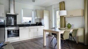 A modern kitchen with white cabinets, a stainless steel range hood, and a dining area with a wooden table and chairs. - Bungalow in Friesland with Outdoor Spa (Friesland)