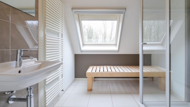 A modern bathroom with a skylight, a wooden bench, and a glass shower enclosure. - Bungalow in Friesland with Outdoor Spa (Friesland)