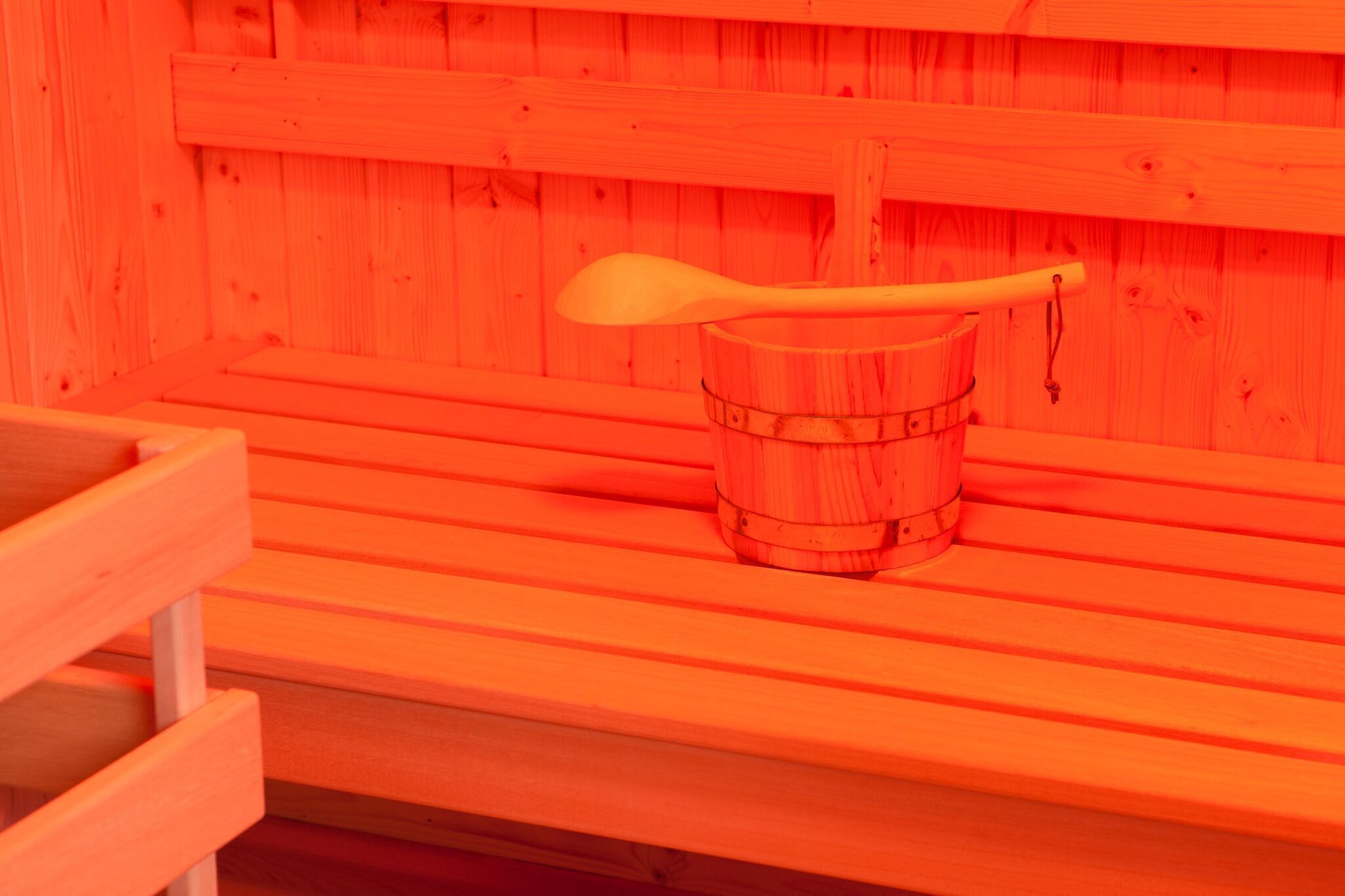 A wooden sauna bench with a wooden bucket and a wooden spoon.