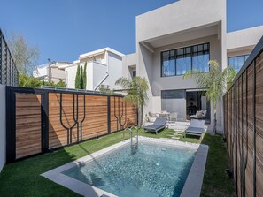 A modern house with a swimming pool, a patio with lounge chairs, and a wooden fence.