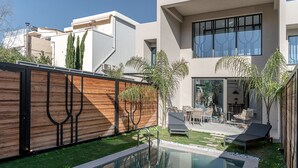 A modern house with a swimming pool, a wooden fence, and a patio area with outdoor furniture. - Urban Oasis - Walking distance to the Old Town, the beach and all kind of shops! (Chania)