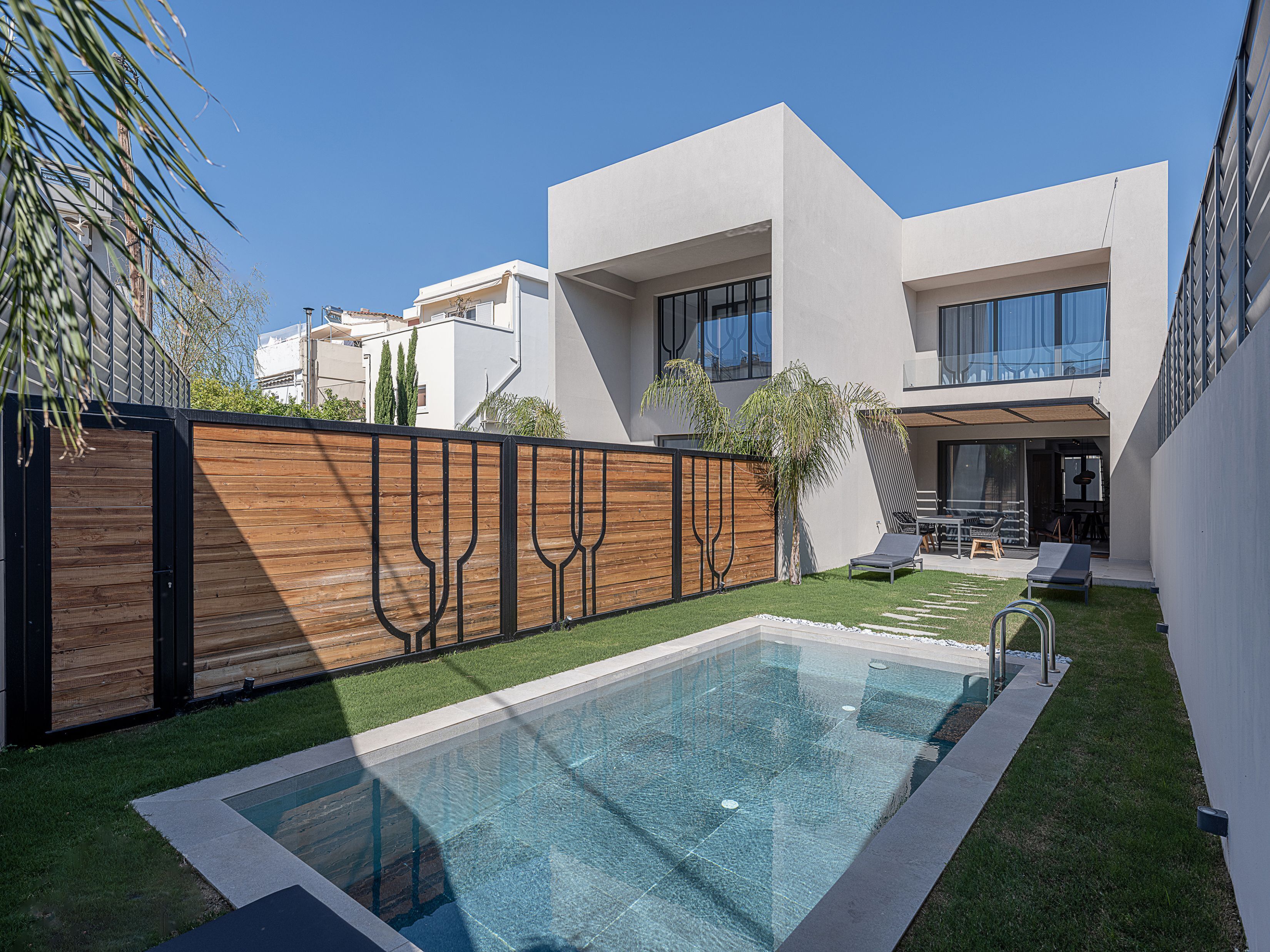 Ein moderner Poolbereich mit einem rechteckigen Pool, einer Holzlattenumzäunung und einem zweistöckigen Gebäude mit großen Fenstern.