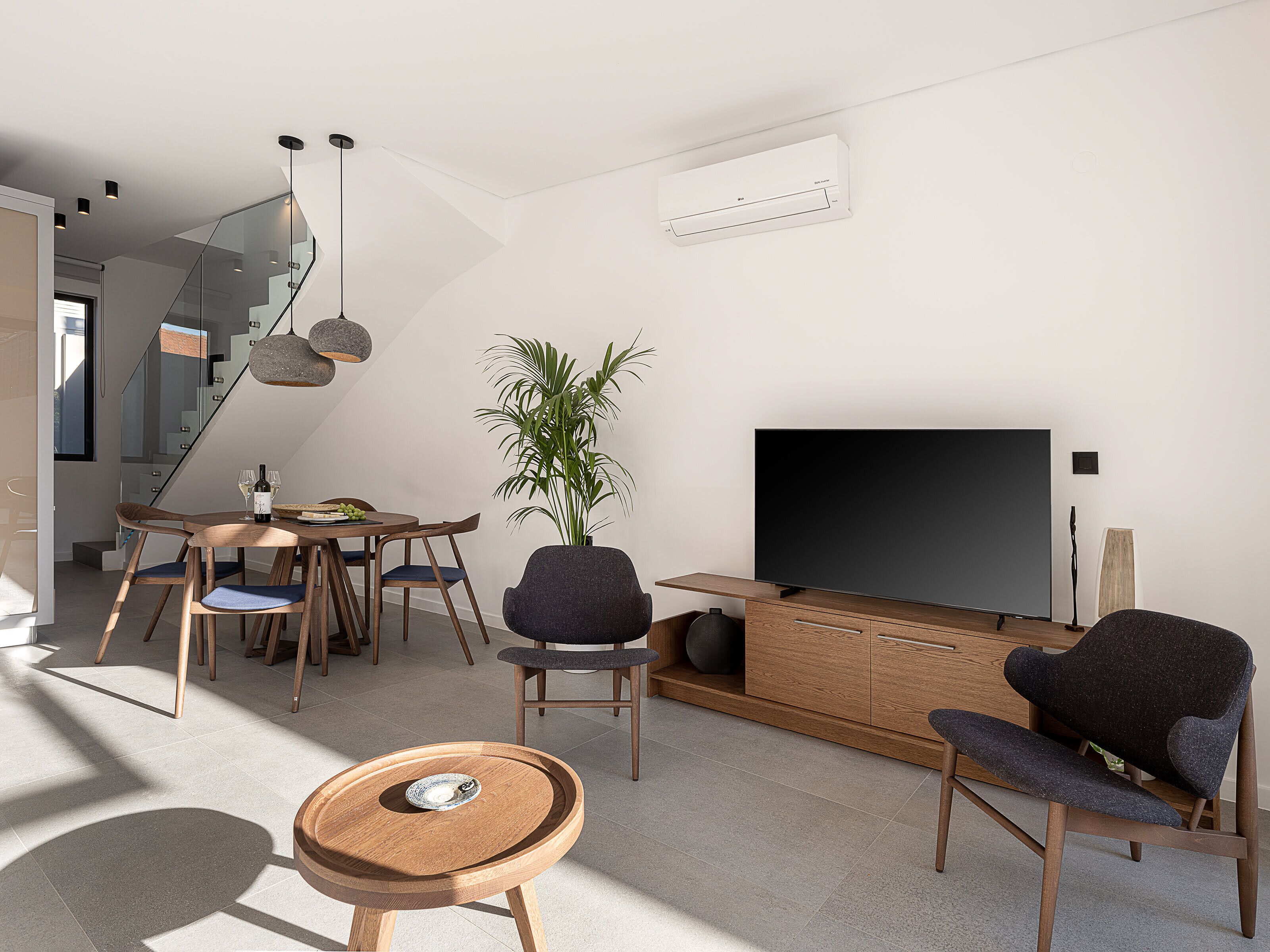 Un soggiorno moderno con una TV a schermo piatto, un'area pranzo con tavolo e sedie, e una scala che conduce a un altro piano.