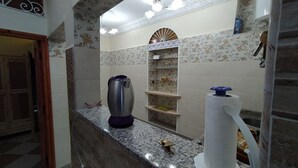 A bathroom with a marble countertop, a sink, a mirror, a towel dispenser, and a shelf with toiletries. - Casa Morisca Classic (Sidi Ifni)
