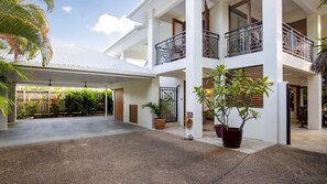 A multi-level building with a covered entrance, potted plants, and a view of the surrounding greenery. - Frangipani Villa | Port Douglas (PORT DOUGLAS)