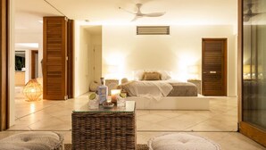 Une chambre moderne avec un grand lit, deux tables de chevet avec des lampes, un ventilateur de plafond et une vue sur l’extérieur grâce à une porte coulissante.