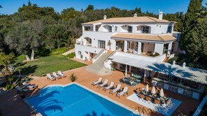 Una casa grande de dos pisos con piscina, mobiliario exterior y un porche cubierto.