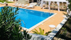 Un edificio de dos plantas con piscina, asientos al aire libre y un área cubierta.