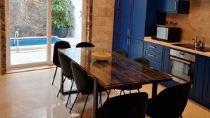 Een moderne keuken met blauwe kastjes, een glazen eettafel en een hanglamp.
