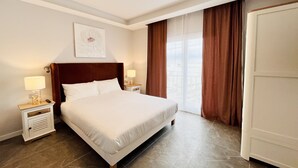 Een hotelkamer met een groot bed, twee nachtkastjes met lampen, een kastje en een raam met gordijnen, evenals een deur.