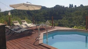 Eine Holzterrasse mit Pool, Liegestühlen und Sonnenschirm.