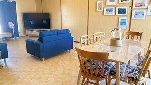 Ein Wohnzimmer mit blauem Sofa, Esstisch aus Holz und Stühlen, einem Fernseher und gerahmten Bildern an der Wand.