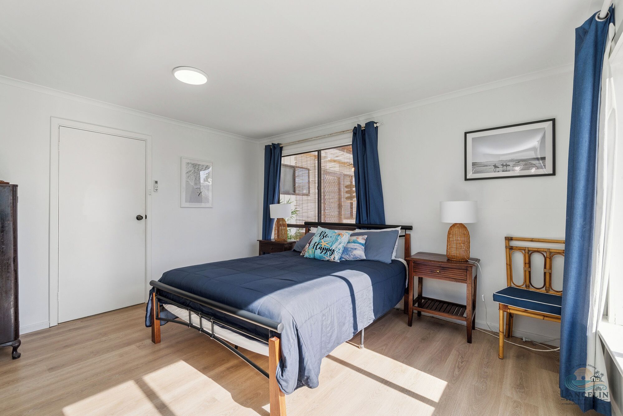 A bedroom with a bed, bedside tables, a chair, a window with curtains, a wall-mounted picture, and a door.