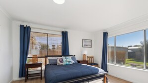Ein Schlafzimmer mit einem großen Bett, einem Fenster mit Vorhängen, einem Nachttisch und einem gerahmten Bild an der Wand.