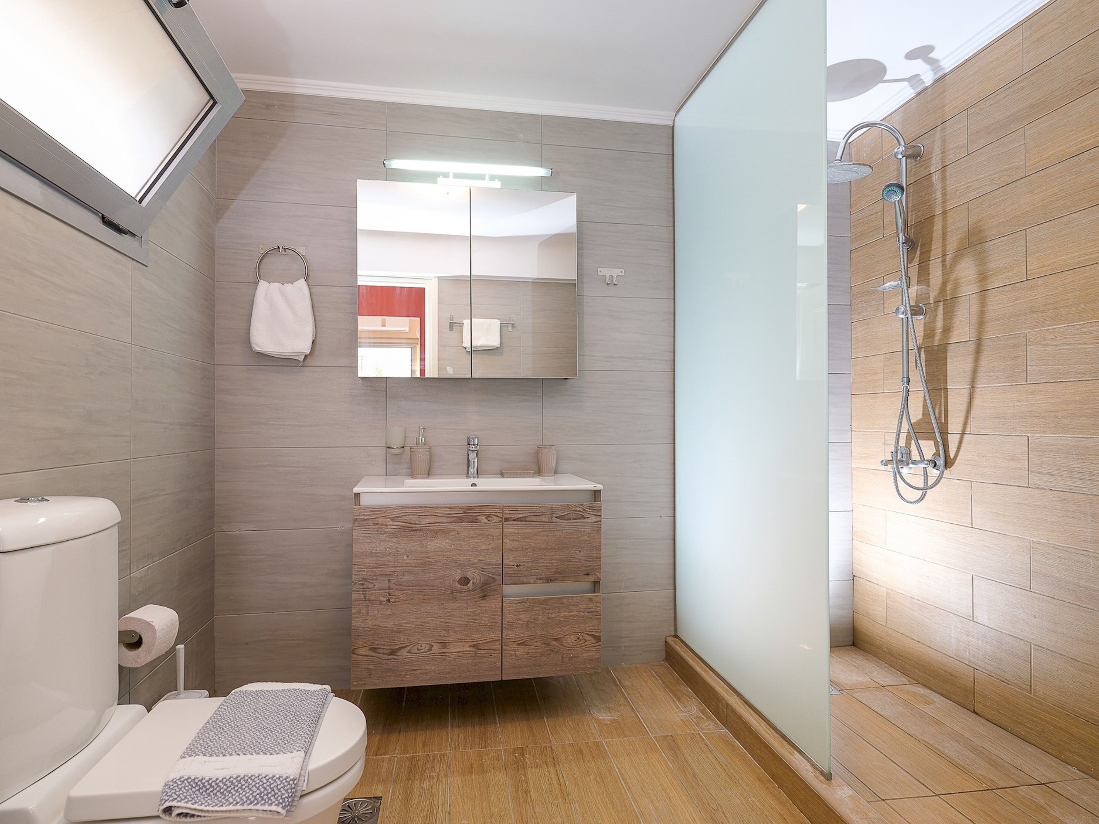 A modern bathroom with a wooden vanity, a toilet, and a shower.