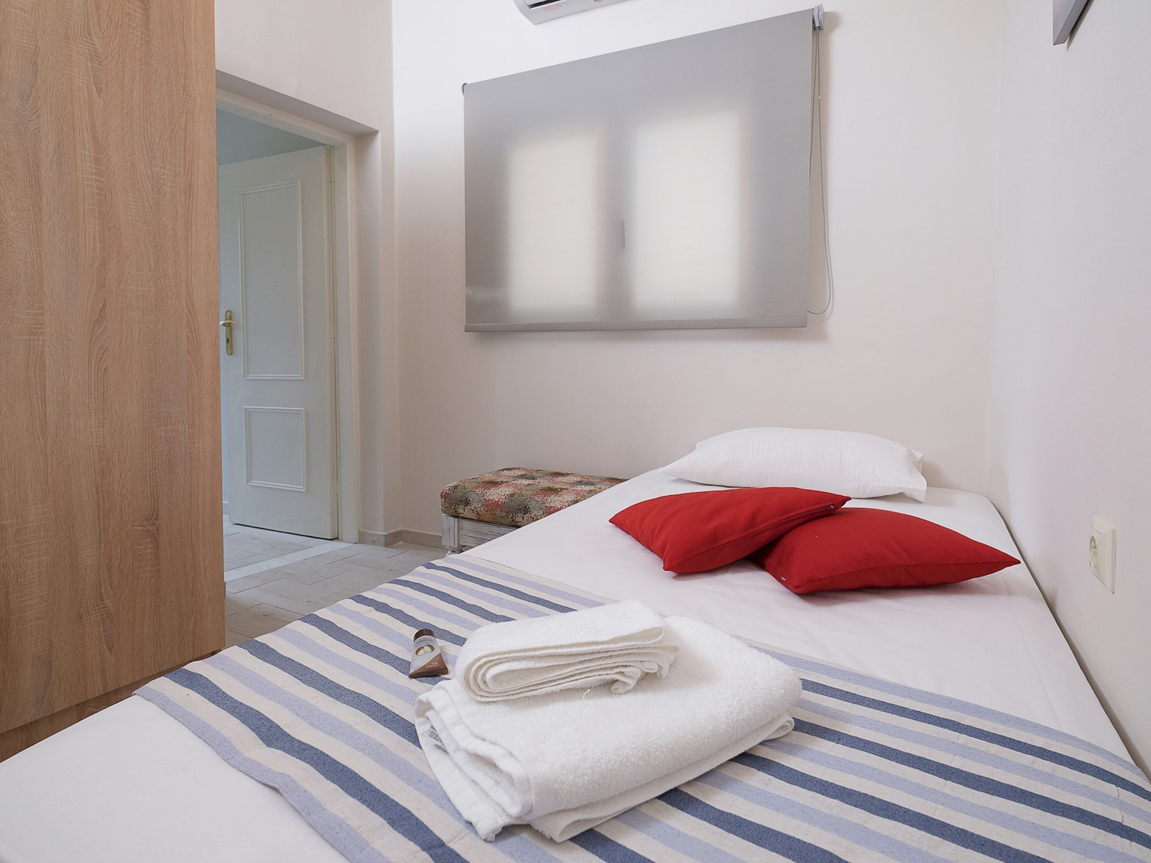A neatly made bed with striped bedding, a small table with a floral tablecloth, and a door leading to another room.