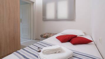 A neatly made bed with striped bedding, a small table with a floral tablecloth, and a door leading to another room.