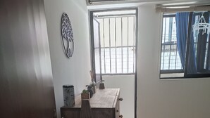 A room with a wooden dresser, a small table with decorative items, a window with curtains, and a bed with a checkered blanket. - Praia de Manaíra (João Pessoa)