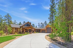 A large, single-story house with a curved driveway, surrounded by trees and a well-maintained lawn.