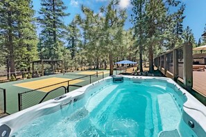 A hot tub surrounded by a fenced area with a basketball court and trees.