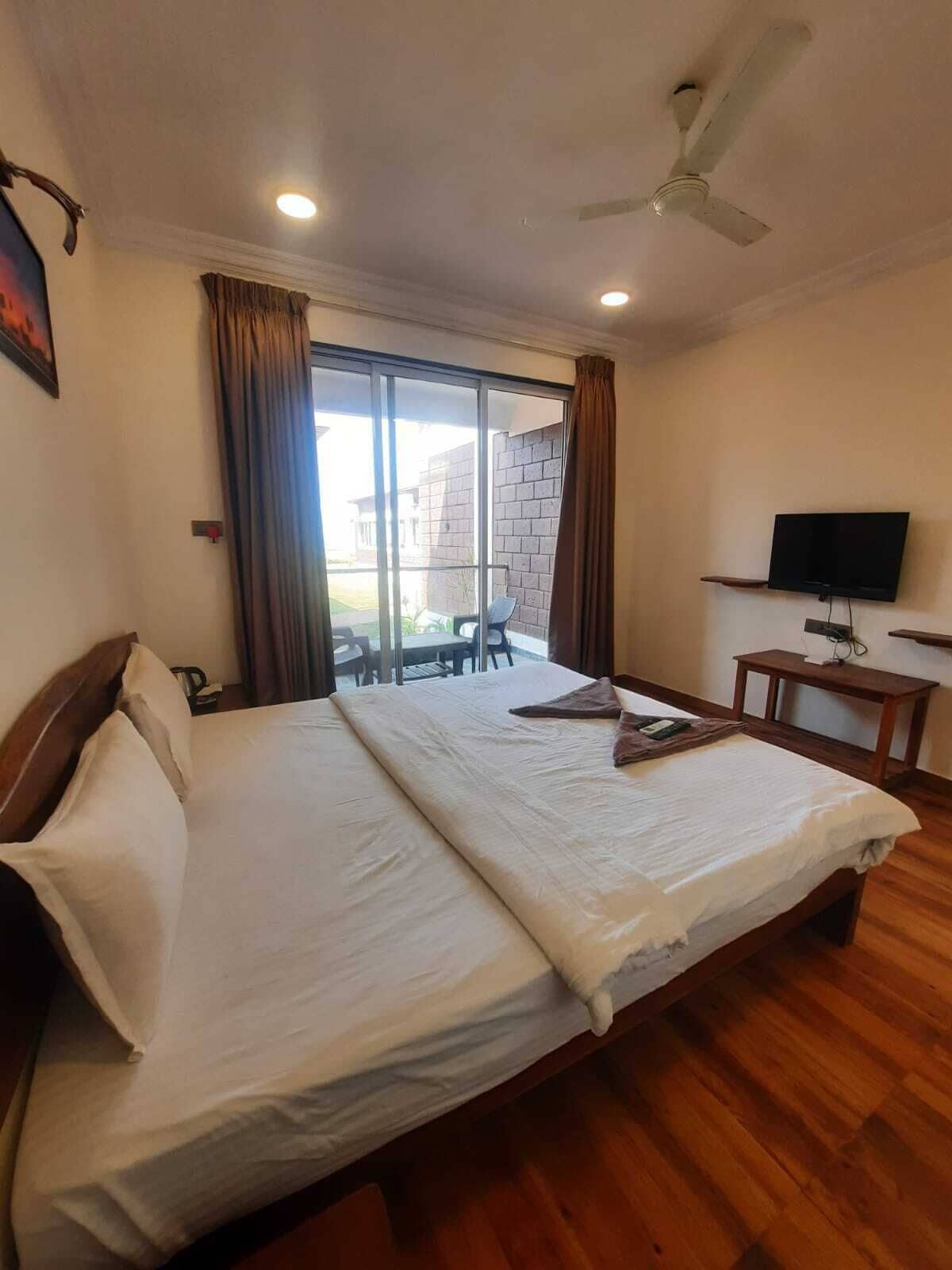 A hotel room with a large bed, a television on a wooden stand, and a sliding glass door to the outside.