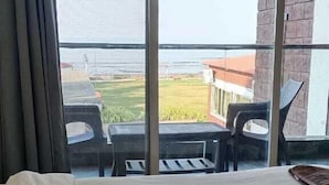 Une chambre d’hôtel avec un lit, de grandes fenêtres et une vue sur un immeuble et la verdure environnante.