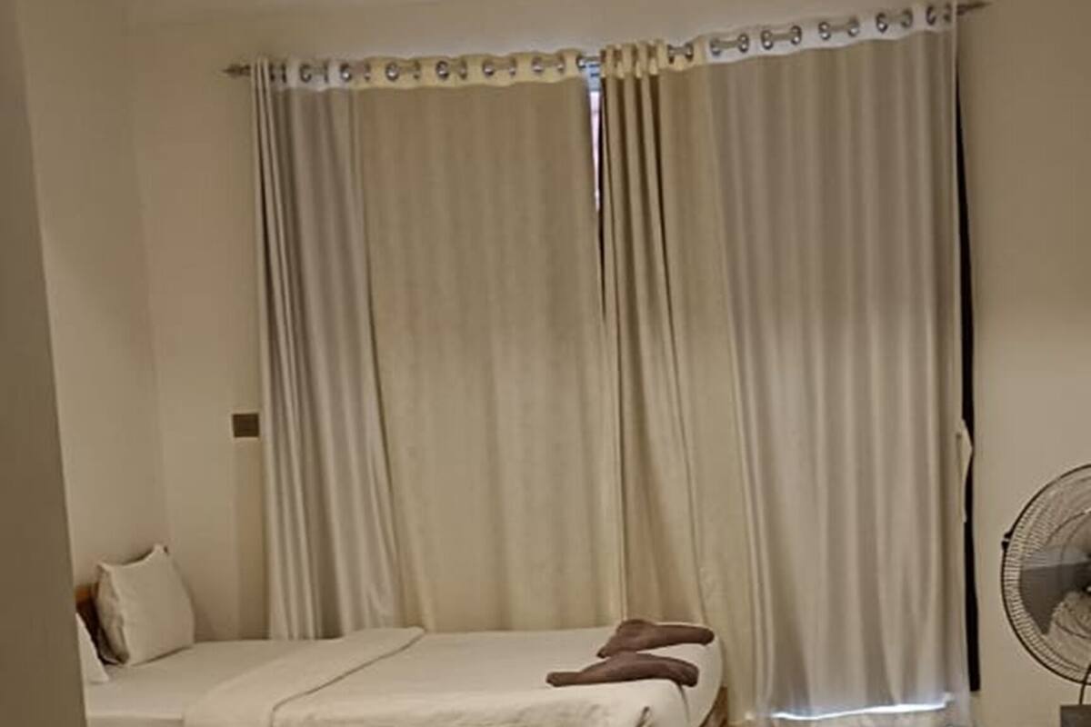 Een hotelkamer met twee bedden, een plafondventilator en uitzicht op de straat.
