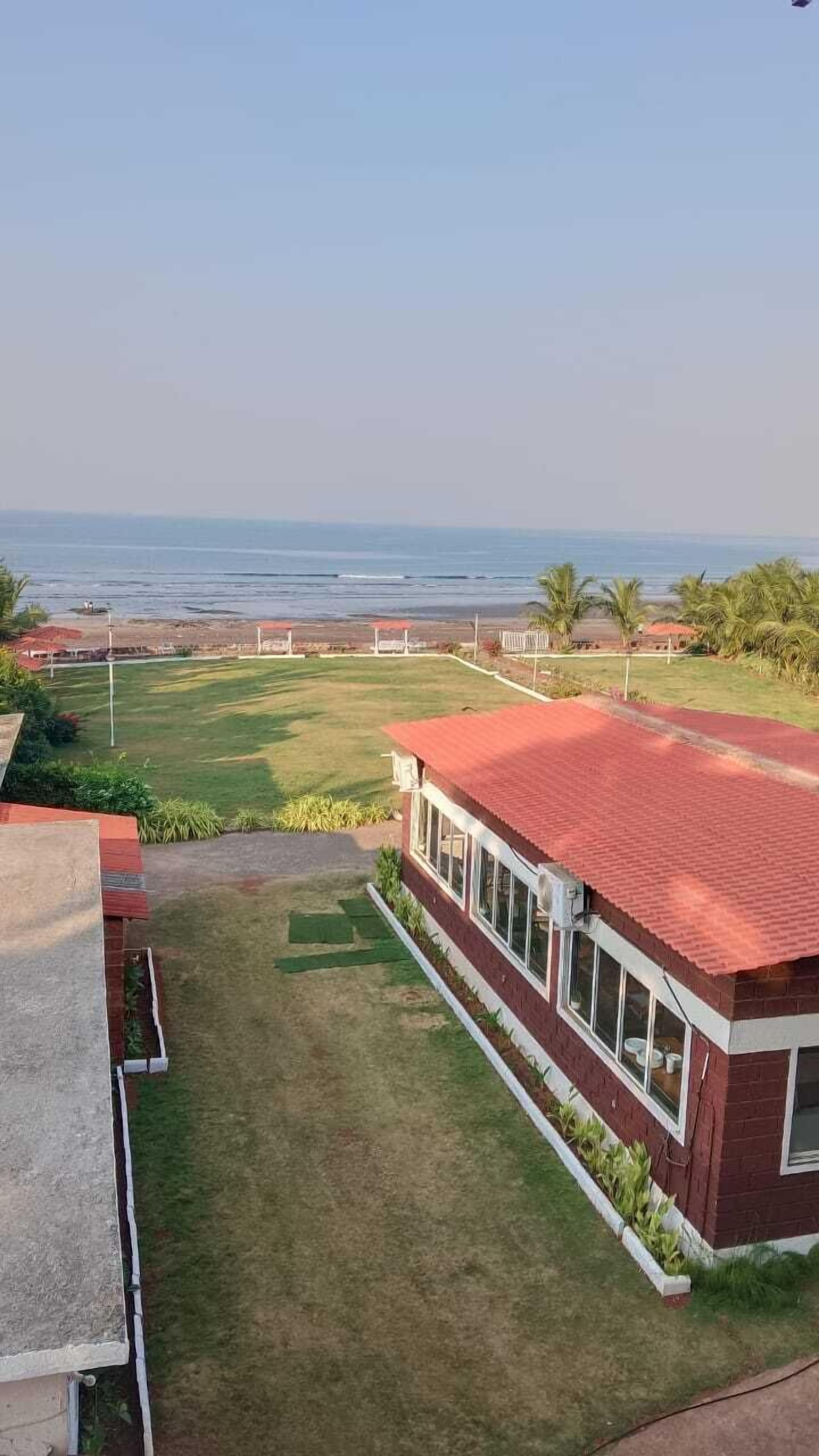 A view of a building with a red roof and large windows, overlooking a grassy area with a view of the ocean.