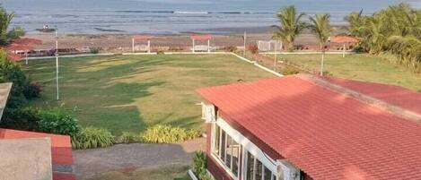 A view of a building with a red roof and large windows, overlooking a grassy area with a view of the ocean.