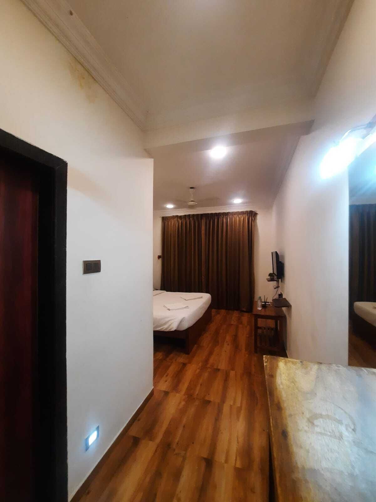 A hotel room with a wooden floor, a bed, a desk, a TV, and a ceiling fan.