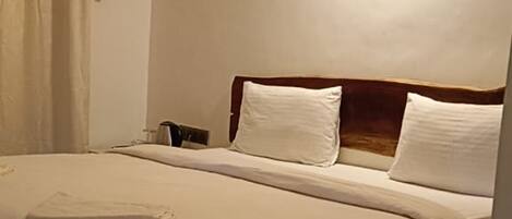 Una habitación de hotel con cama, mesita de noche, luz empotrada en la pared y ventana con cortinas.