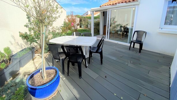 A patio with a table and chairs, a potted plant, and a sliding glass door leading to a covered area. - Charming Cottage with Garden, Near Beach & Town - La Tranche-sur-Mer (La Tranche-sur-Mer)