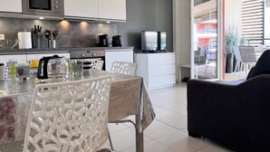 A modern kitchen with white cabinets, a microwave, coffee maker, and a TV. There is a dining area with a table and chairs. - Modern Apartment with Pool, Terrace, and A/C Near Beach - Le Lavandou (Le Lavandou)