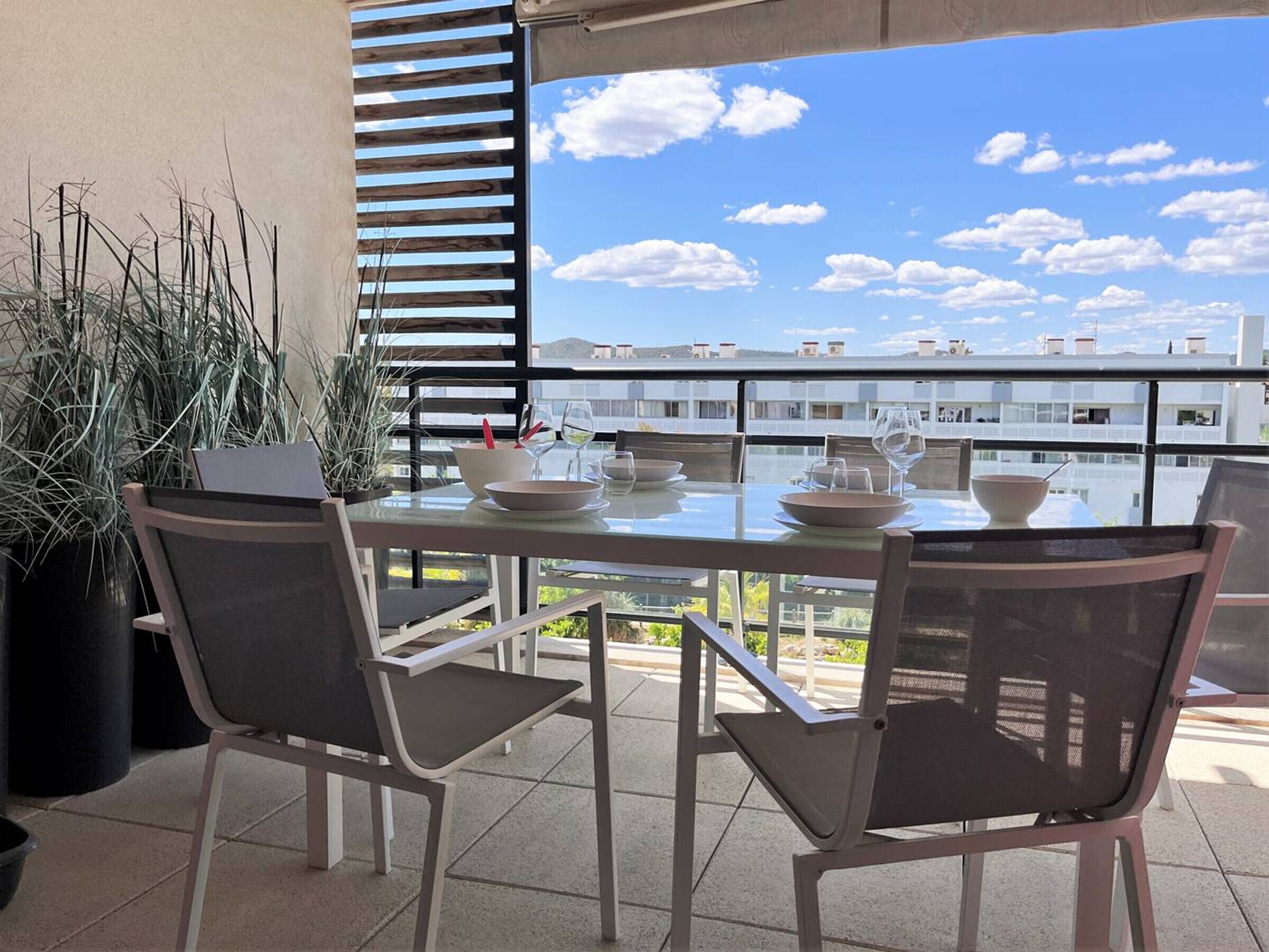 A dining area with a table set for two, chairs, and a view of buildings through a window.