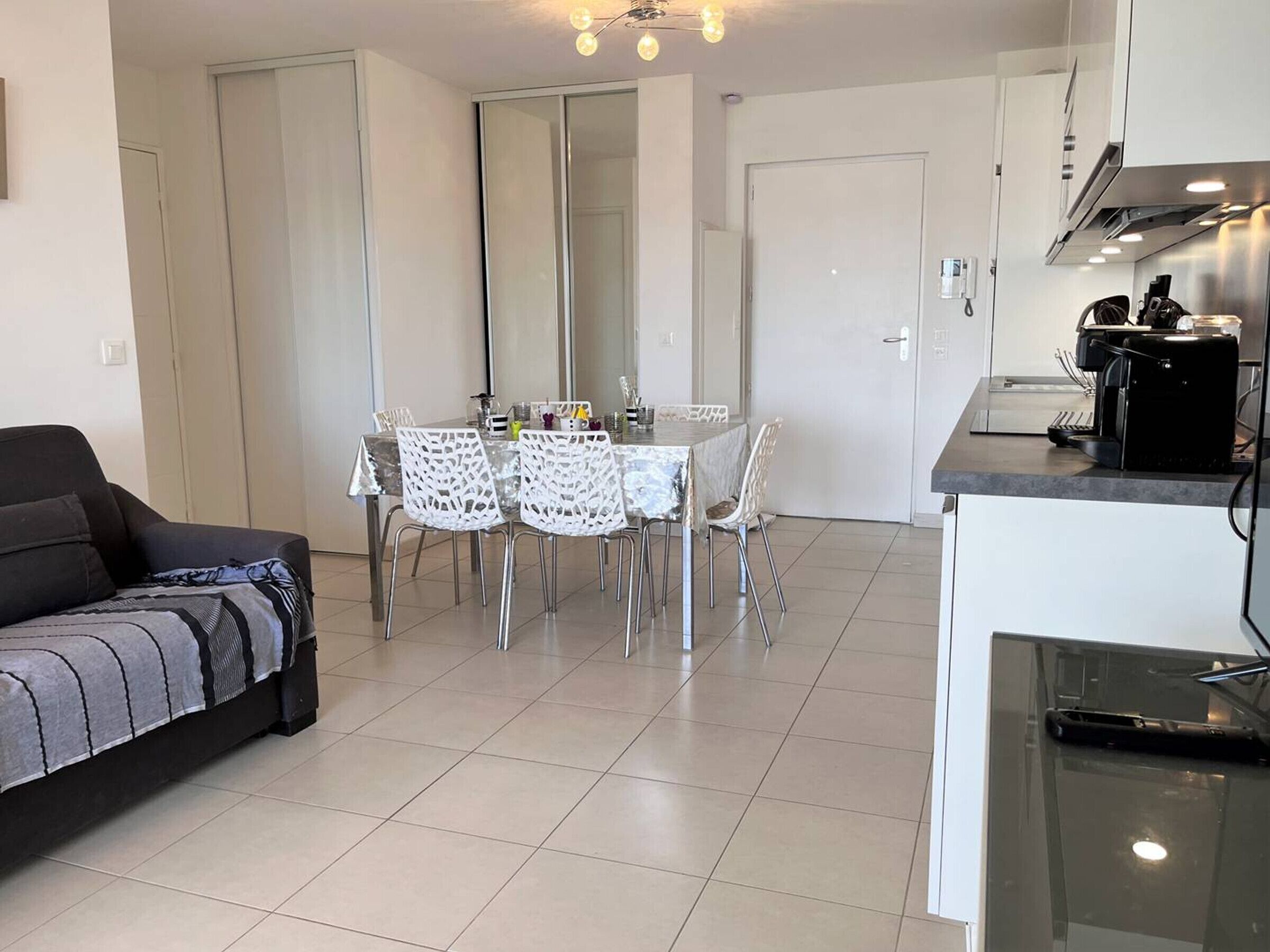 A modern kitchen with a dining area, including a table with chairs, a sofa, and a coffee machine.
