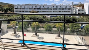A modern building with multiple floors, a balcony with a glass railing, and a clear blue sky with clouds. - Modern Apartment with Pool, Terrace, and A/C Near Beach - Le Lavandou (Le Lavandou)
