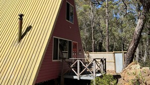 A red cabin with a yellow roof, a wooden deck, and a small porch.