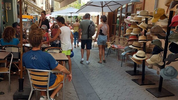 An outdoor café with tables and chairs under umbrellas, a street lined with shops, and a variety of hats displayed outside. - Large cozy studio in Castellane /Gorges du Verdon (Castellane)