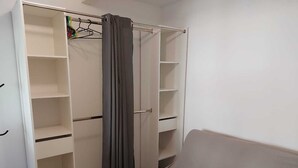 A walk-in closet with multiple shelves and hanging space, a grey curtain, and a white bed. - Large cozy studio in Castellane /Gorges du Verdon (Castellane)